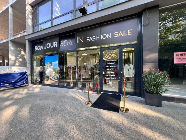 Außenansicht des Bonjour Berlin High Fashion Geschäfts. Das Schaufenster ist stilvoll dekoriert mit Designerstücken von Dolce & Gabbana. Die elegante Fassade zieht Kunden an und spiegelt den exklusiven Charakter des Geschäfts wider.
